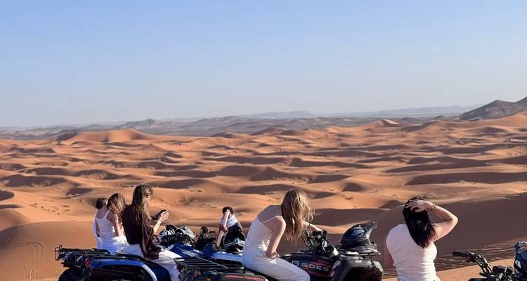 Group of women on quad bikes admire vast rolling sand dunes of the Sahara under a clear sky.