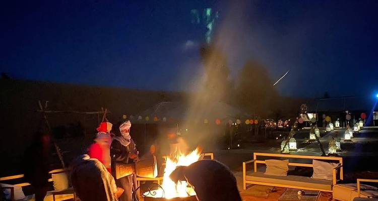 Night desert camp scene with people gathered around a bright campfire under a dark sky.