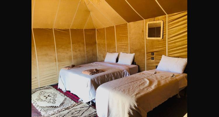 Intérieur d'une tente de campement du désert avec deux lits soigneusement faits, un tapis à motifs et un éclairage doux.