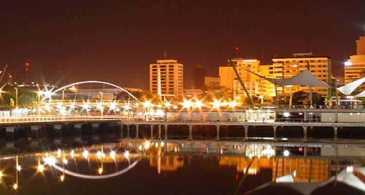 Las luces de la ciudad y los arcos del puente reflejados en la orilla tranquila durante la noche oscura.