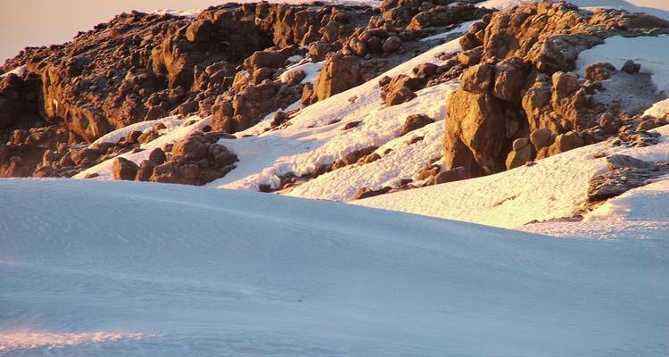 La luz dorada ilumina rocas volcánicas escarpadas cubiertas de nieve en las alturas del Monte Kilimanjaro