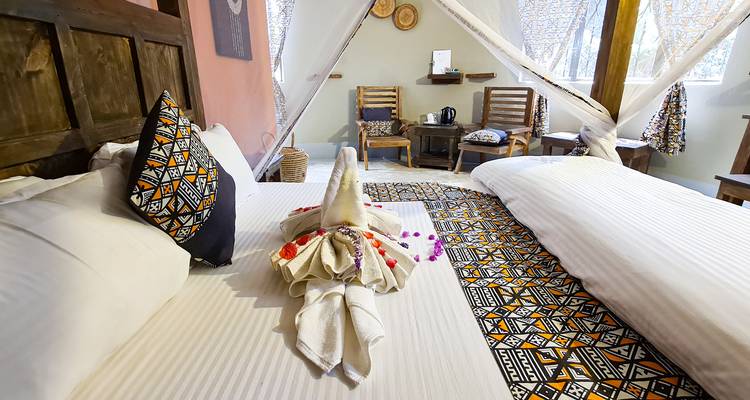 Elegante dormitorio de cabaña con camas gemelas, textiles estampados y arte con toallas en el centro.