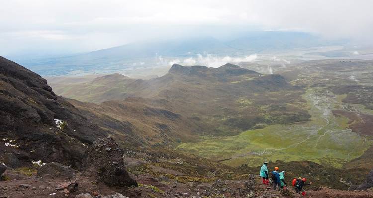 Trekkers tackle a steep volcanic ridge high above patchwork valleys and drifting cloud vapor.