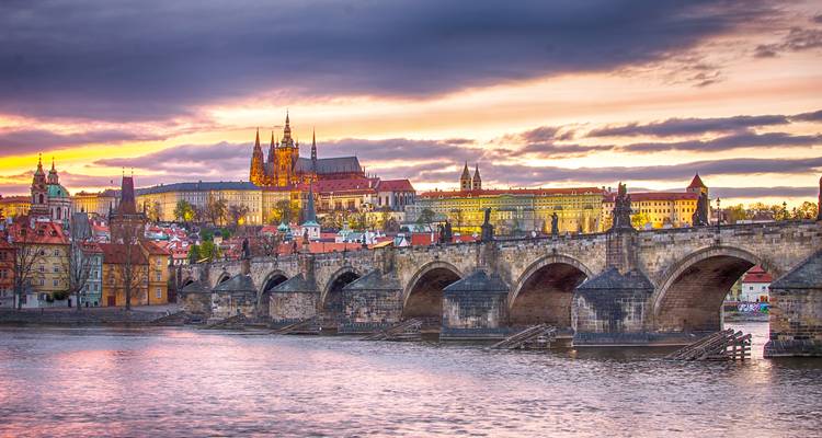 Pont Charles enjambant la rivière Vltava avec le château de Prague illuminé par un coucher de soleil dramatique