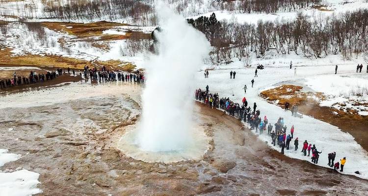 Les foules entourent le geyser Strokkur lors de son éruption à travers un sol couvert de neige en hiver.