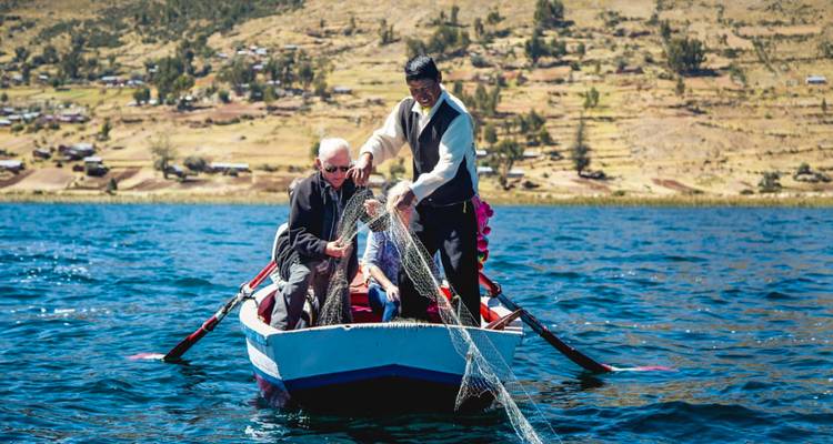 Un pêcheur local aide un visiteur à remonter un filet d'une petite barque sur le lac scintillant.