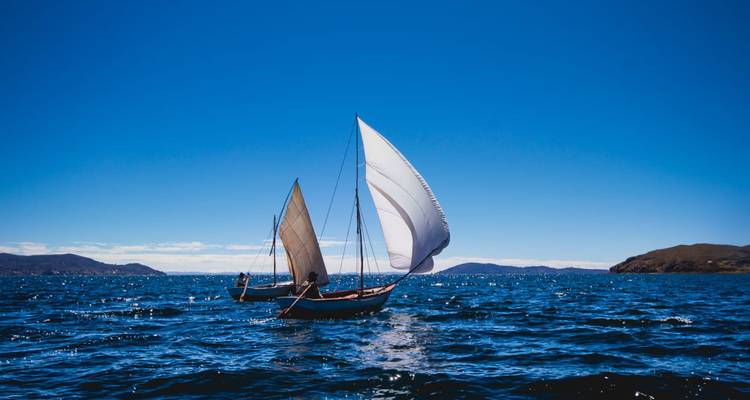 Deux élégants voiliers glissent sur les eaux bleu foncé du lac Titicaca sous un ciel impeccable.