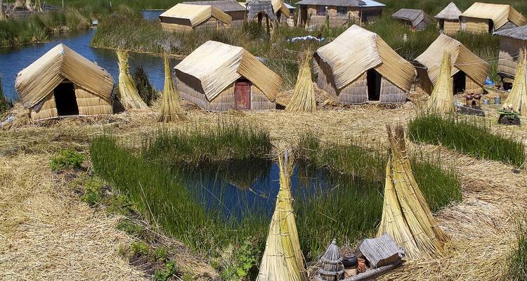 Gros plan de huttes de roseaux et de piles de totora entourant un petit lagon sur une île flottante.