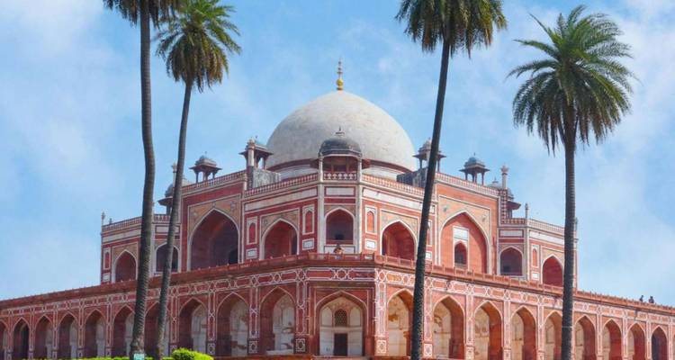Magnificent red-sandstone mausoleum with white marble dome framed by tall palm trees against a clear sky.