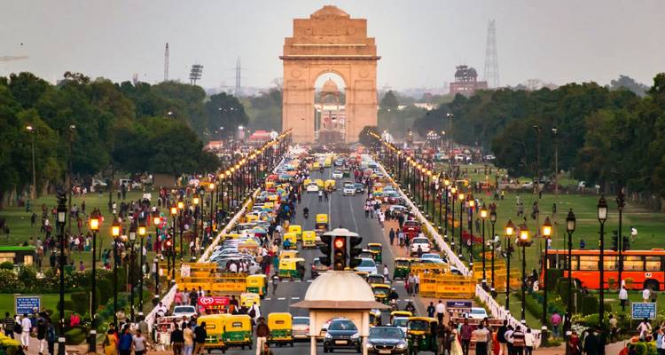 Busy ceremonial avenue leading to India Gate crowded with vehicles, pedestrians and glowing street lamps at dusk.