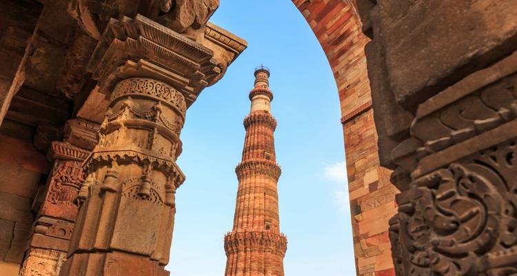 Towering Qutub Minar seen through intricately carved stone archways under a bright blue sky.