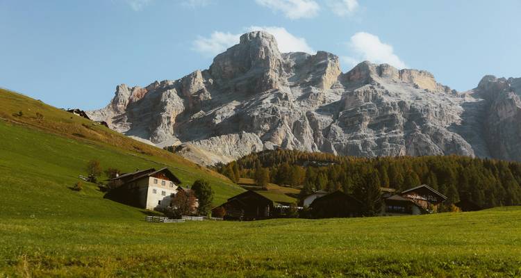 Charmants alpages parsemés de fermes sous un imposant pic calcaire dans les Dolomites.