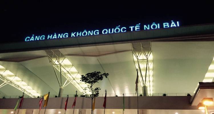 Plan extérieur de nuit du terminal de l'aéroport international de Noi Bai avec signalétique vietnamienne illuminée.