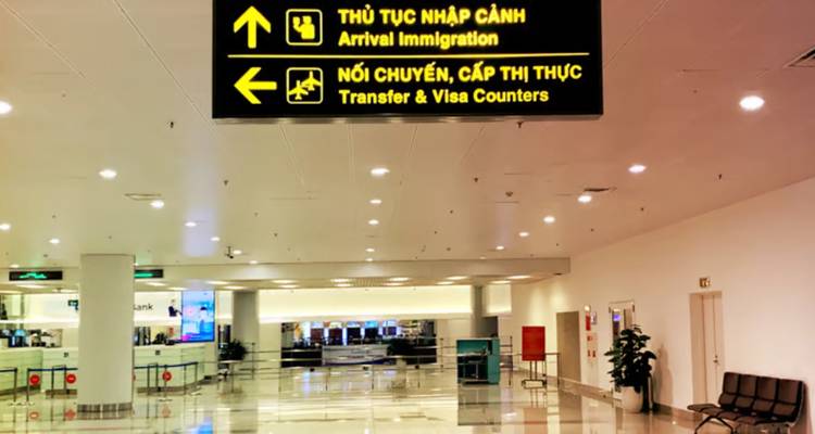 Couloir intérieur d'aéroport avec panneaux directionnels jaunes bilingues vers l'immigration et les comptoirs de transfert.