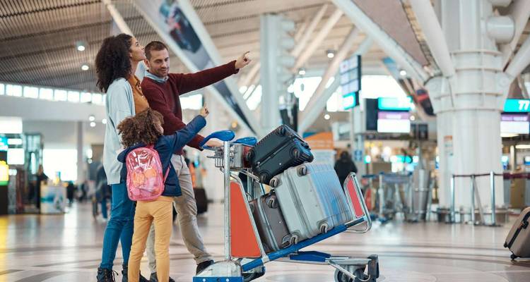 Famille avec chariot à bagages consulte les panneaux d'affichage dans un terminal d'aéroport moderne et lumineux