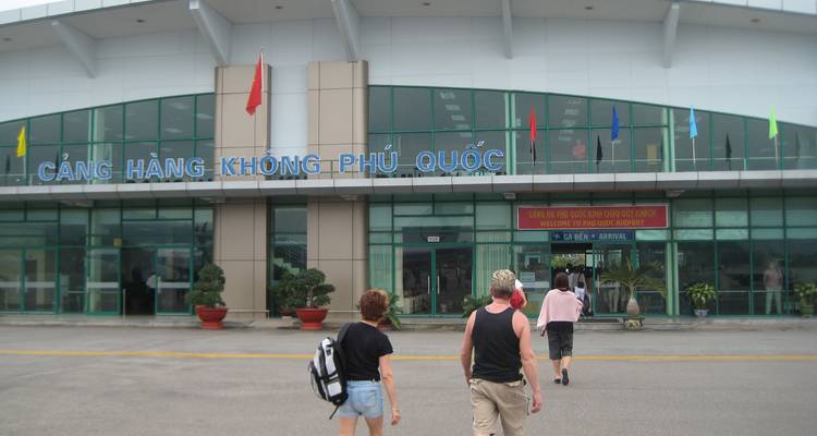 Travelers walk toward the glass entrance of Phu Quoc Airport marked with Vietnamese signage.