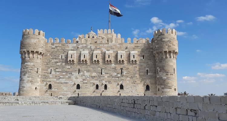 Fortaleza costera de piedra con bandera egipcia contra un cielo azul brillante