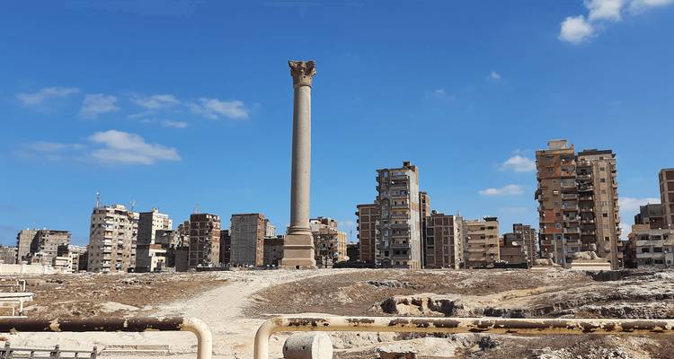 Columna antigua y alta que se alza frente a bloques de apartamentos modernos en un día soleado