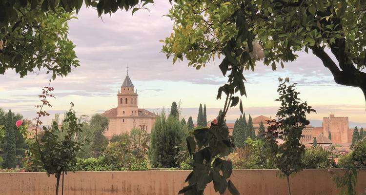 Sanftes Morgenlicht über Granadas Alhambra, eingerahmt von Gartenlaub und fernen Bergen.
