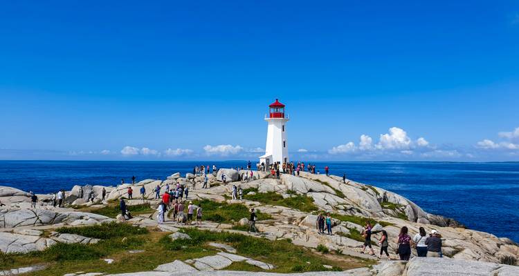 Menigten die de granieten rotspunt en helderrode vuurtoren van Peggy's Cove verkennen op een heldere dag