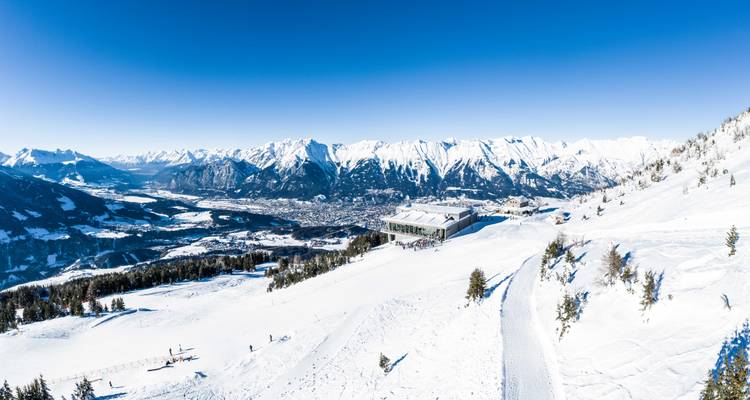 Weitläufiges verschneites Alpenpanorama offenbart Innsbruck, das weit unten unter einem strahlend blauen Winterhimmel eingebettet liegt.