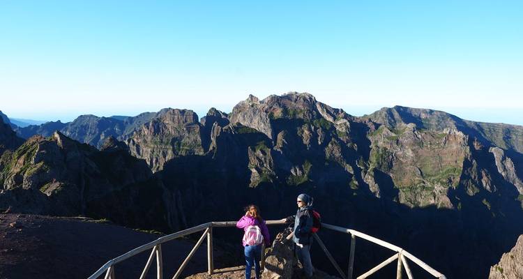 Twee wandelaars staan bij een houten uitkijkpunt met ruige bergtoppen die erachter oprijzen.
