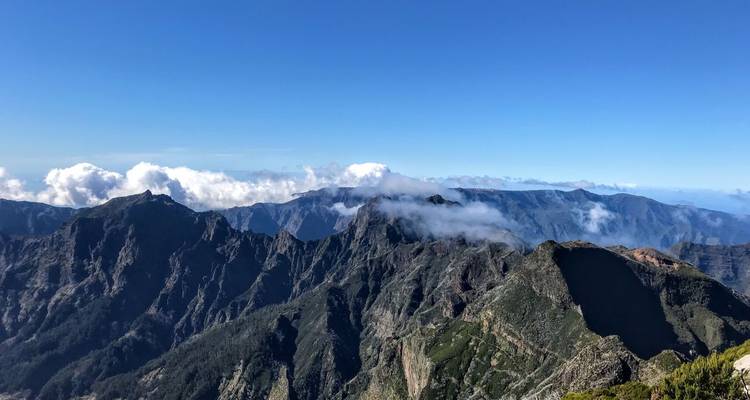 Panoramisch uitzicht op ruige bergkammen onder een heldere blauwe lucht met verspreide wolken.
