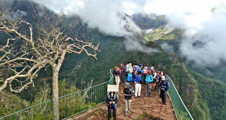 Een groep trekkers staat op een uitkijkplatform hoog boven met wolken gevulde bergdalen.