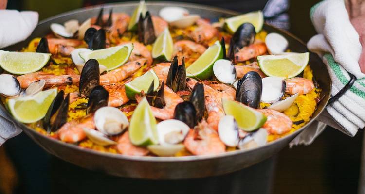 Nahaufnahme einer bunten Meeresfrüchte-Paella voller Garnelen, Muscheln, Venusmuscheln und Limettenspalten.