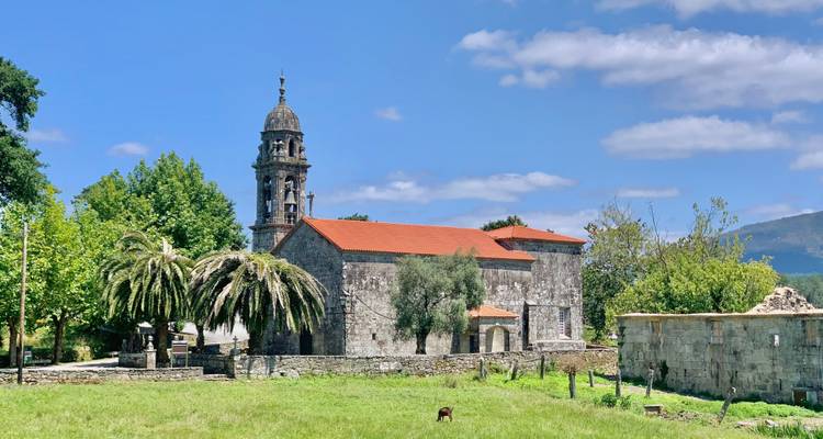 Ländliche Steinkirche mit einem Glockenturm steht auf einer grasbewachsenen Wiese unter strahlend blauem Himmel.