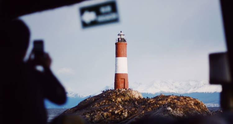 Silhouette d'une personne prenant une photo du phare depuis le cadre d'une fenêtre de bateau.