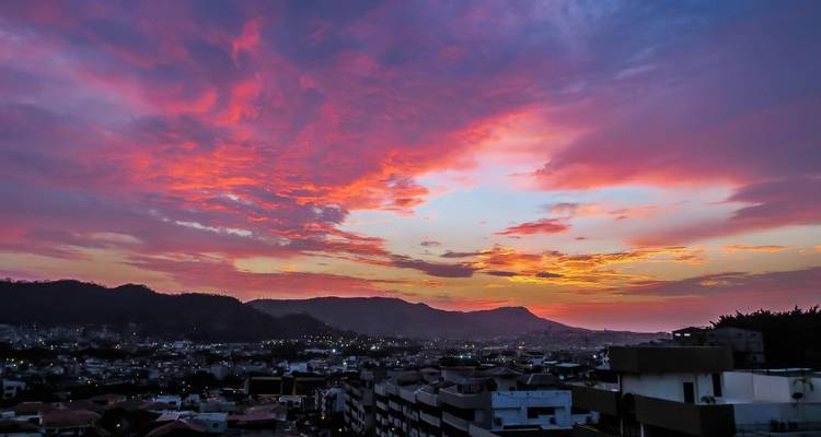 Nubes vibrantes del atardecer sobre los tejados de la ciudad y colinas distantes en Guayaquil