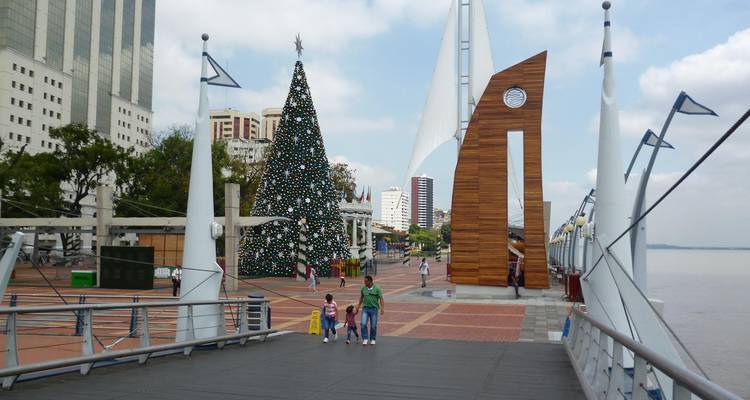 Familia caminando por un malecón junto al río decorado con un árbol de Navidad gigante y esculturas modernas