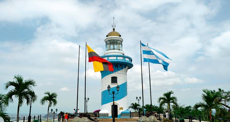 Faro azul y blanco con banderas ecuatorianas en la cima del cerro Santa Ana bajo un cielo parcialmente nublado