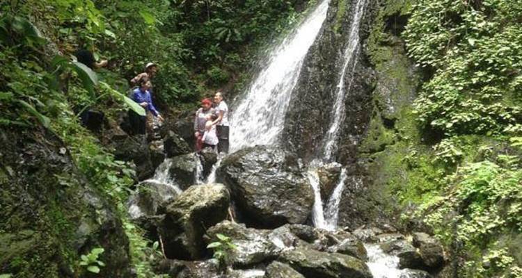 Travelers stand beside a small jungle waterfall cascading over mossy rocks.