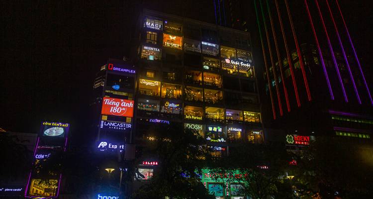 Nachtansicht eines hell erleuchteten Hochhauses voller Cafés und Neonschilder in Ho-Chi-Minh-Stadt.