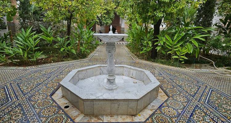 Ruhiger Riad-Innenhof mit Marmorbrunnen, umgeben von üppigem Grün und gemusterten Fliesen.