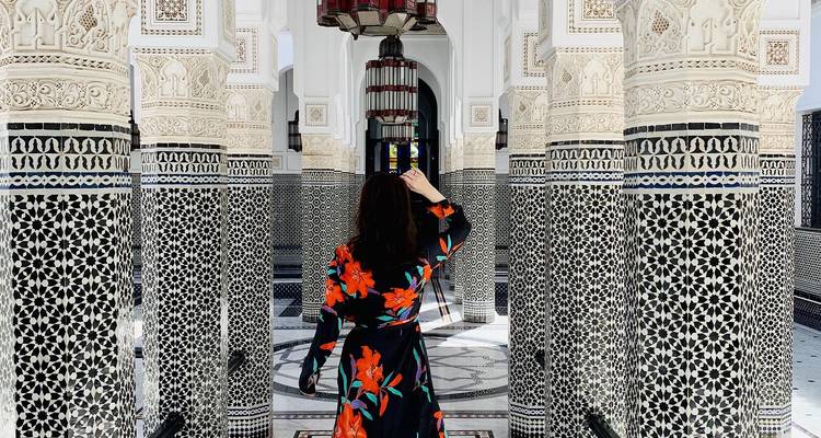 Woman in floral dress wanders through a lavish Moorish-style interior with elaborately tiled columns.