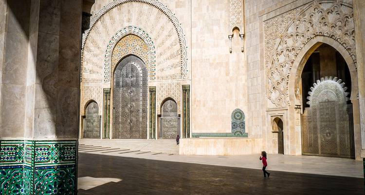 Grand courtyard of Casablanca’s Hassan II Mosque bathed in sunlight, showcasing immense ornate doors and mosaic details.