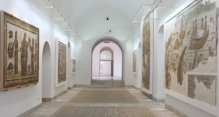 Bright corridor in the Bardo Museum lined with ancient mosaics and arched doorways.