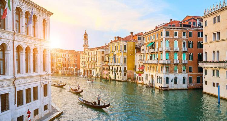 Gran Canal besado por el sol con góndolas deslizándose entre coloridos palacios en Venecia.