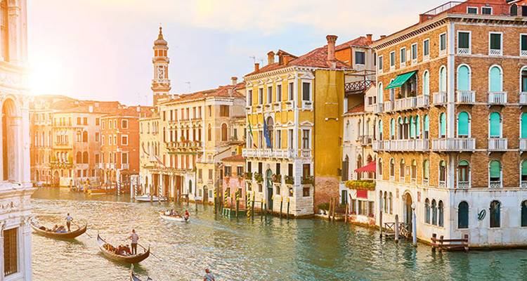 Sonnenbeschienener Canale Grande in Venedig, gesäumt von bunten Palästen, während Gondeln durch das Wasser gleiten.