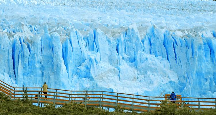 Des visiteurs sur une passerelle éclipsés par l'imposante face bleue d'un glacier en Patagonie.
