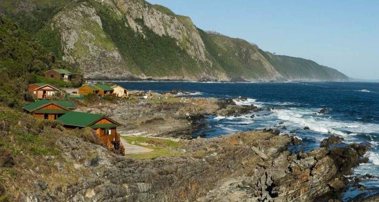 Côte sauvage avec des cottages en bois surplombant les vagues bleues déferlantes et les montagnes boisées.