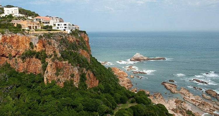 Falaises marines orange surmontées de villas modernes surplombant un océan calme et vaste.