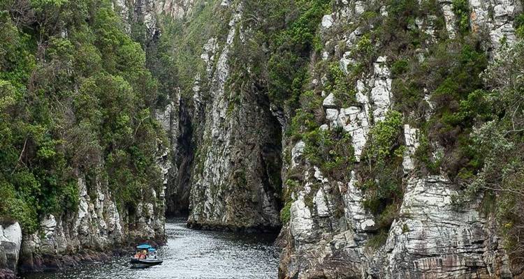 Petit bateau avec passagers glissant à travers un canyon étroit spectaculaire aux parois rocheuses abruptes et à la végétation luxuriante.