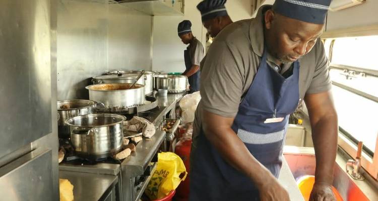 A cook prepares meals in a stainless-steel kitchen inside a train’s dining car.