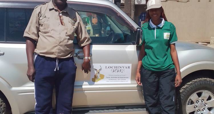 Two safari guides stand beside a 4x4 bearing a Lochinvar Safaris logo under bright sunshine.