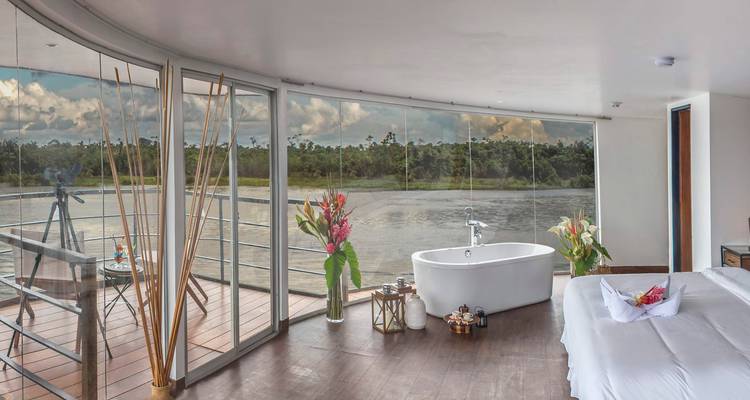 Suite de luxe dotée d'une baignoire îlot et de baies vitrées panoramiques donnant sur une rivière de jungle.