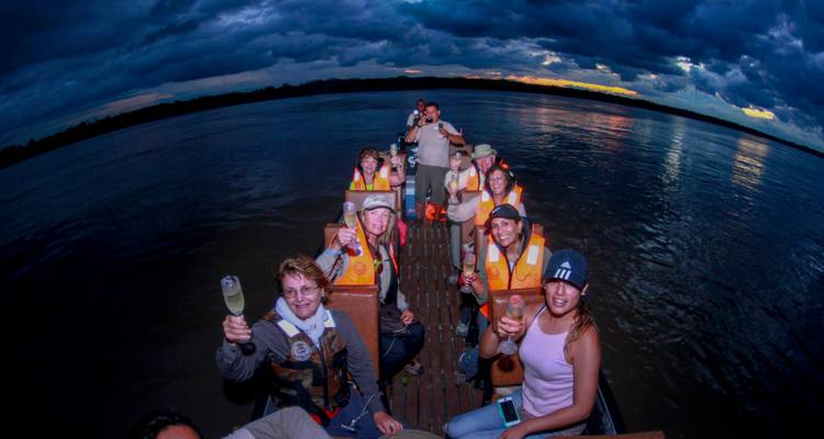 Des voyageurs lèvent leurs verres de champagne sur le pont d'un petit bateau au crépuscule sous des nuages dramatiques.